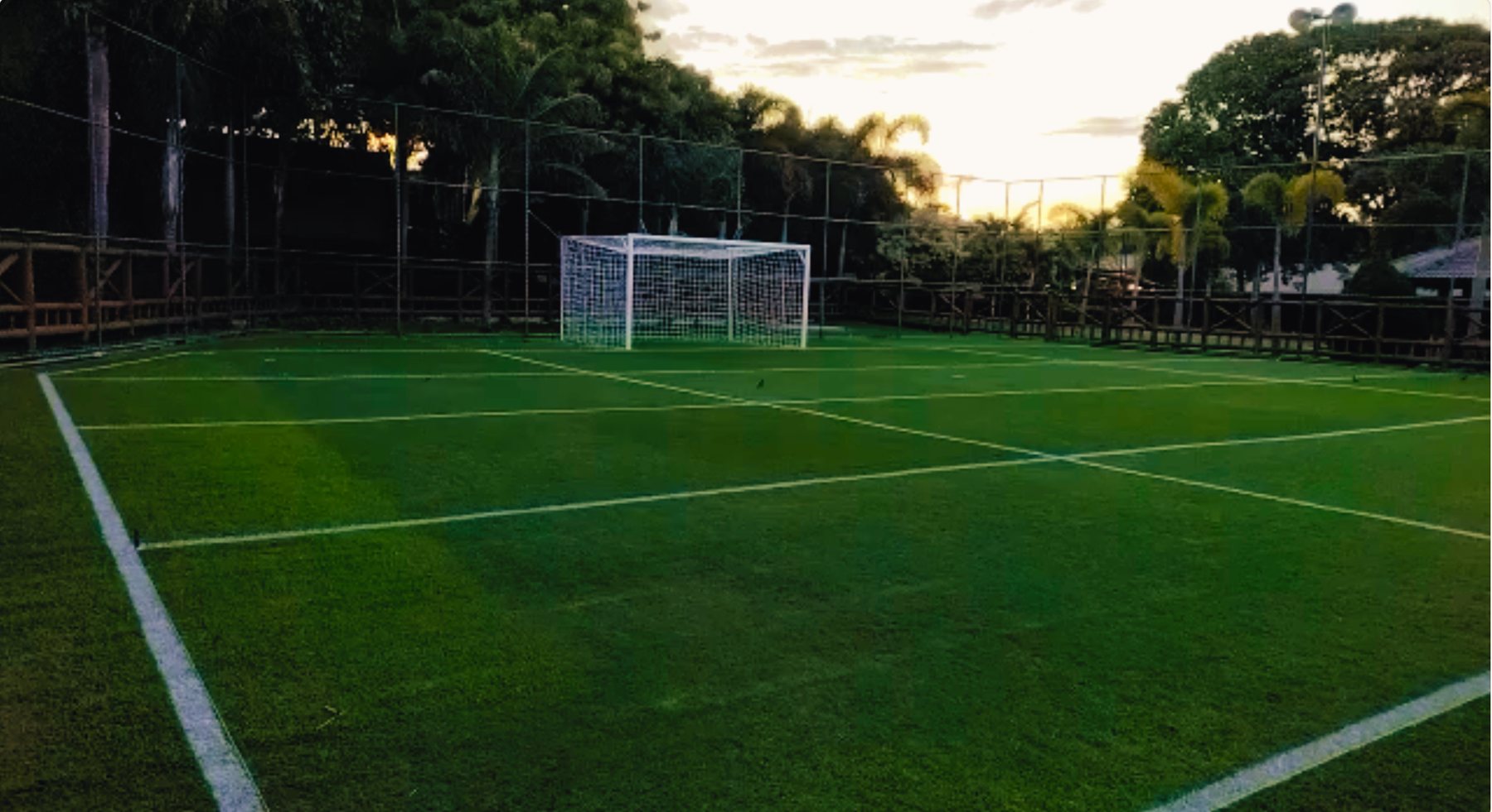 Campo de grama cercado do Sítio Chuin ao entardecer, com trave e palmeiras ao fundo